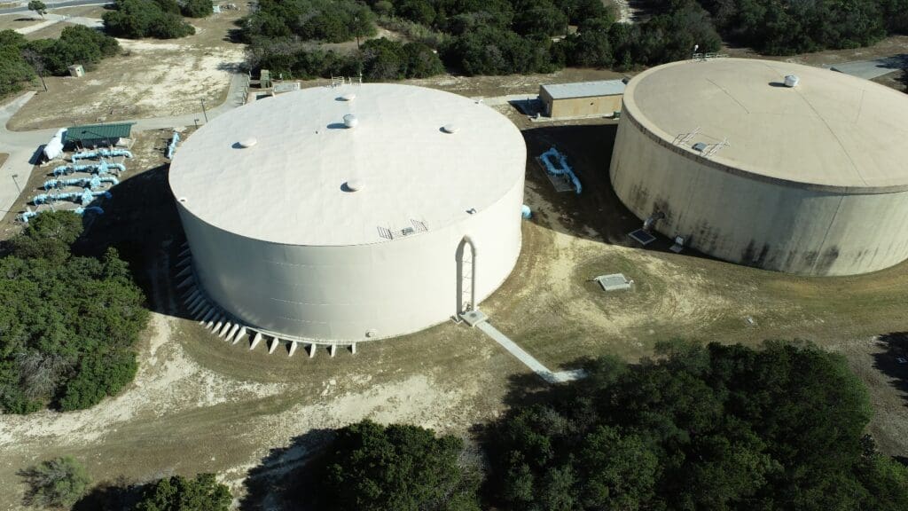 An aerial view of two large tanks in a wooded area.