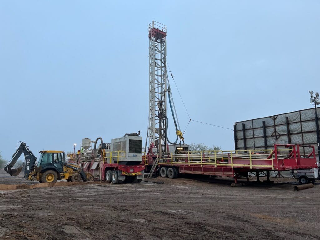 A drilling rig in a field with a tractor.