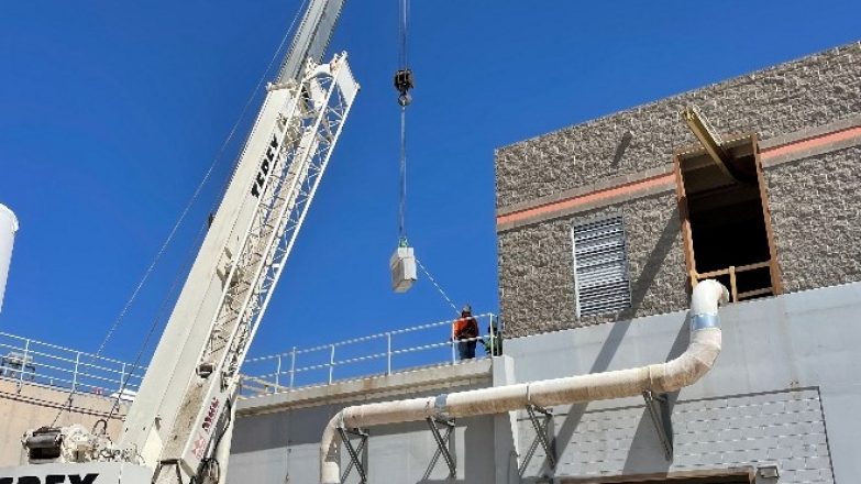A crane lifts a large truck in front of a building.