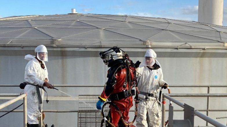 A group of people in protective suits standing on top of a tank.